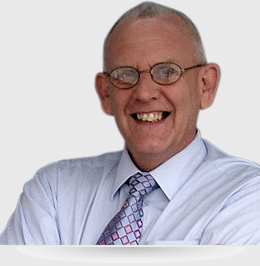 A man with glasses and a tie smiling.