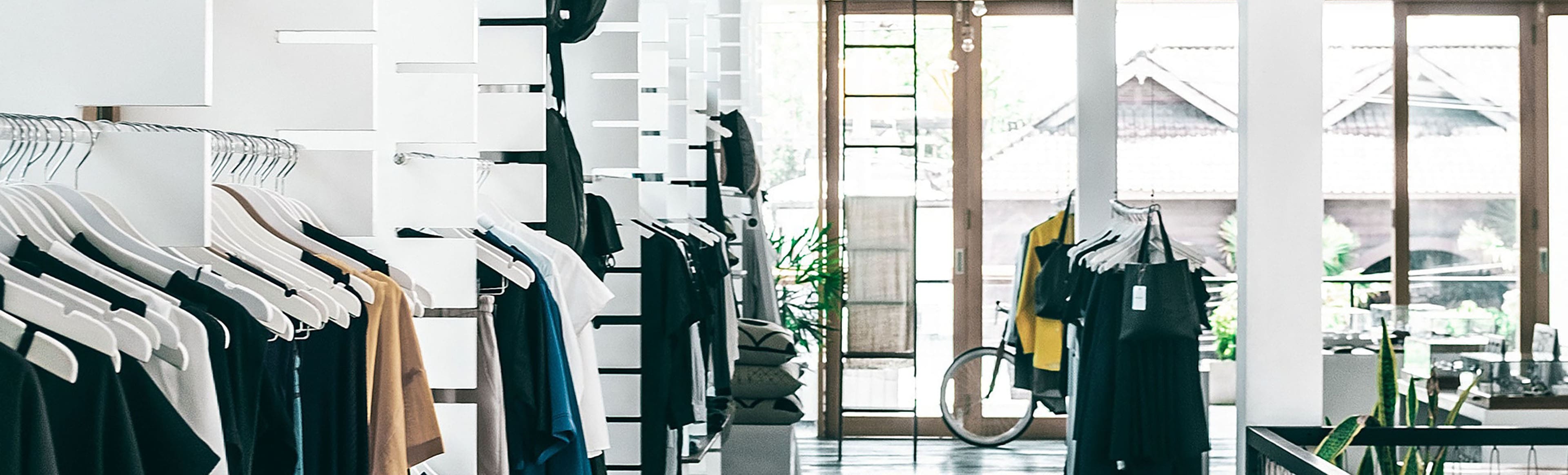 A bicycle parked in front of a store with clothes on the racks.