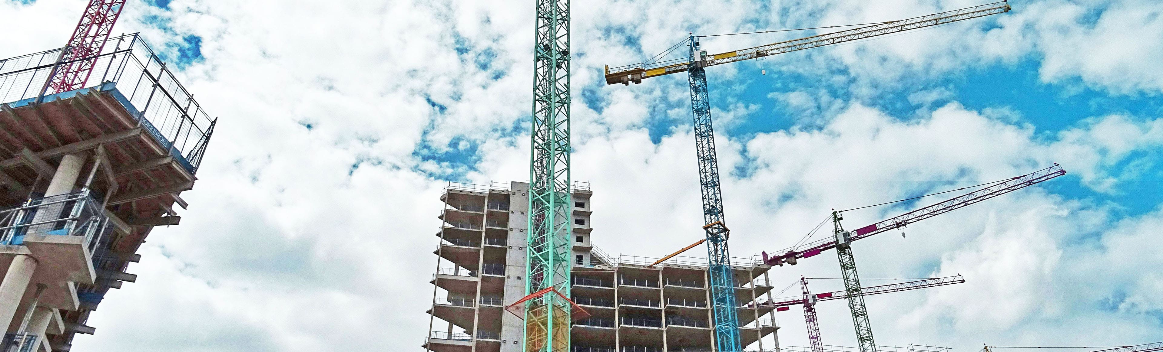 A building under construction with two cranes in the foreground.